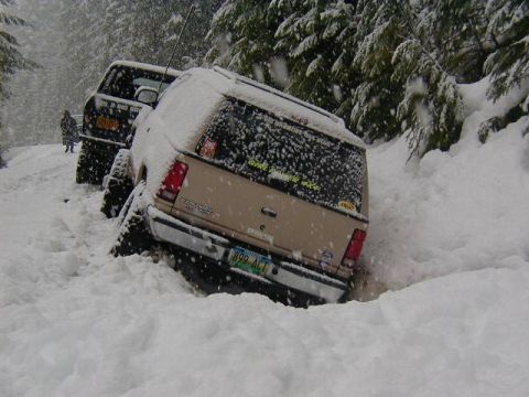 1994 Ford Explorer - Two vehicles are stuck in deep snow on a wooded trail during a snowfall.