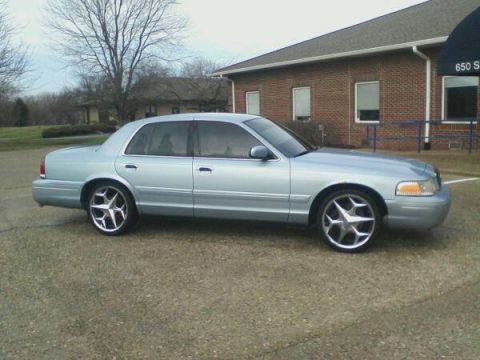 2000 Mercury Grand Marquis - A light blue sedan is parked in front of a brick building with a blue railing.
