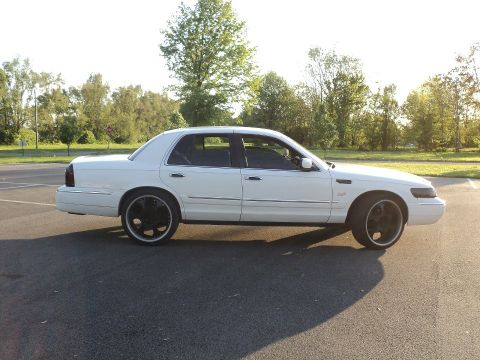 2000 Mercury Grand Marquis - Side profile of a white 2000 Mercury Grand Marquis sedan with custom black rims parked outdoors.