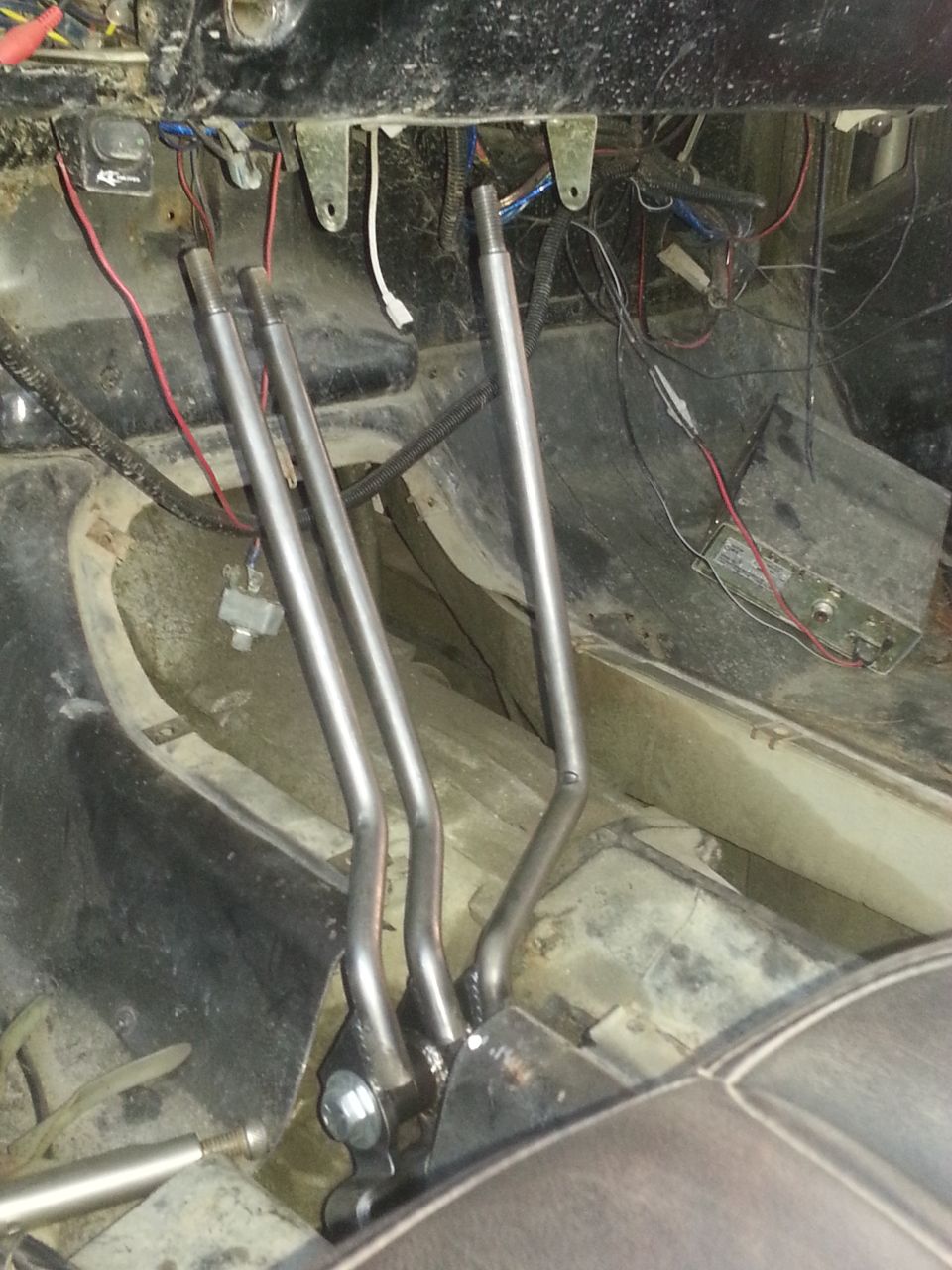 Three bare-metal shift levers on the stripped floorpan of a truck cab interior