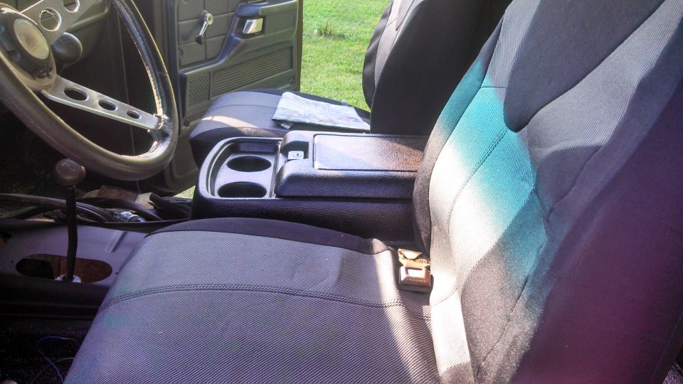 Interior view of a vehicle, showing the steering wheel, dashboard, center console with cup holders, and seats