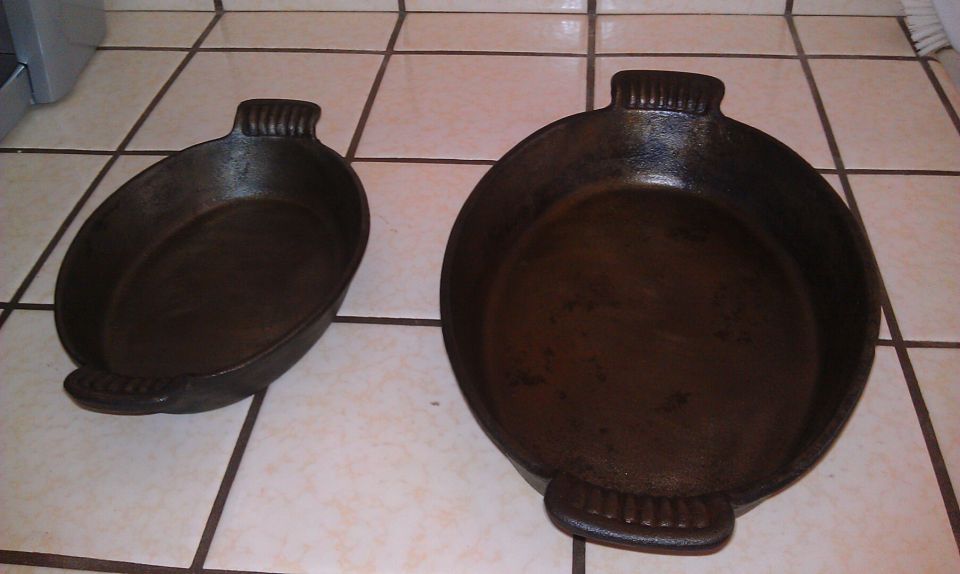 Two cast iron skillets, one oval and one round, on a tiled surface