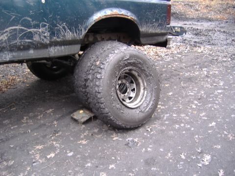 1988 Ford Bronco - Muddy truck tire on a block, showing rust on the wheel well.