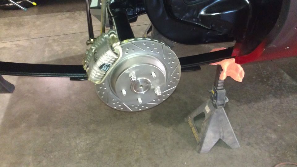 Rear brake rotor with drilled holes and silver caliper, part of a vehicle suspension system on jack stands