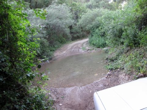 1992 Ford Explorer - A vehicle approaches a water crossing on a dirt road through a wooded area.