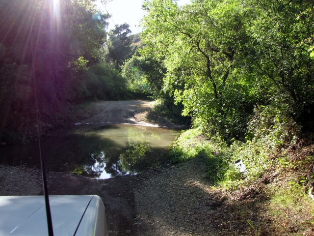 White SUV driving through shallow stream on dirt road
