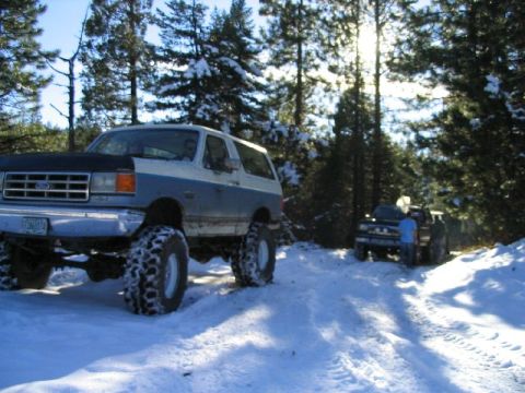 1988 Ford Bronco - A lifted Ford Bronco navigates a snowy trail with another truck following.