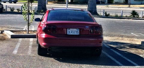 1995 Ford Mustang - Rear view of a red 1995 Ford Mustang parked in a lot, showing its distinctive taillights and license plate.