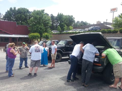 1986 Ford Bronco - Several people gather around a dark green Ford Bronco with its hood open in a parking lot.