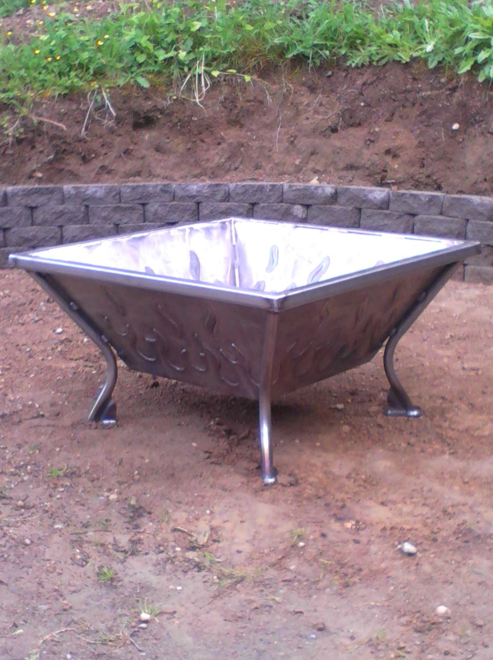 Metal fire pit with decorative flame cutouts and four curved legs, viewed from a 3/4 angle