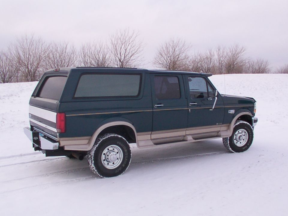 Dark green four-door Ford Bronco conversion with topper parked in a snowy field