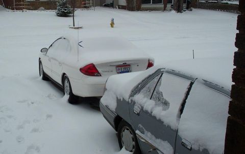 2001 Ford Taurus - Two cars are parked in a snowy driveway, partially covered by snow.