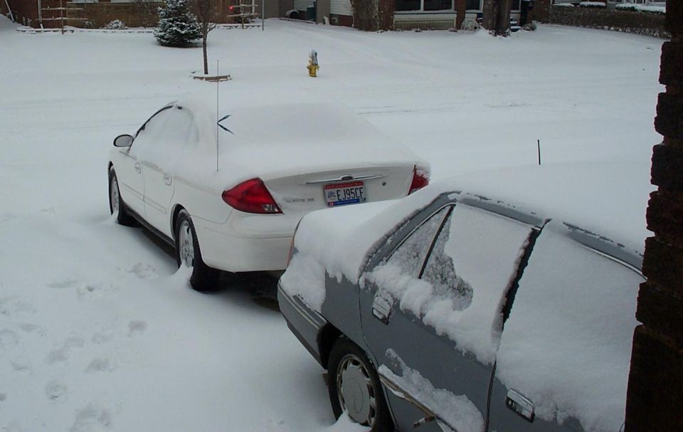 White Ford coupe and snow-covered car in a snowy driveway