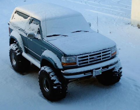 1996 Ford Bronco - A snow-covered Ford Bronco with oversized tires sits in a snowy landscape.