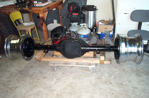 1995 Ford Bronco - A complete rear axle assembly with center differential housing resting on a wooden pallet in a garage, a chrome wheel mounted at each end;…
