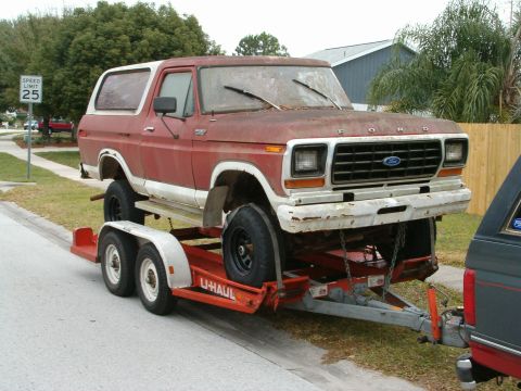 1979 Ford Bronco - A weathered red and white Ford Bronco is loaded onto a U-Haul trailer, ready for transport.