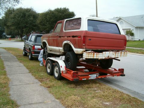 1979 Ford Bronco - A red and white 1979 Ford Bronco is seen being transported on a trailer, with another vehicle parked alongside.