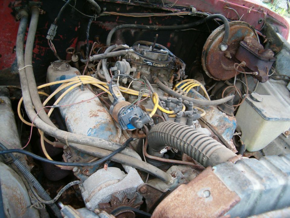 Rusty V8 engine bay with Carter AFB carburetor and yellow plug wires in a red vehicle
