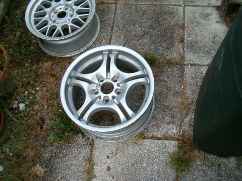 1991 Ford Bronco - Two alloy wheels are shown resting on a paved surface with some grass and dirt around them.