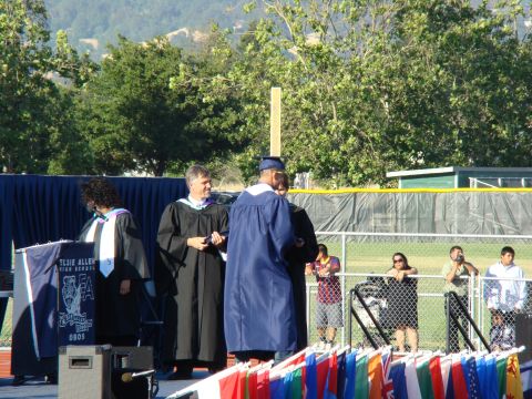 1989 Ford Bronco - Graduation ceremony with students and faculty on stage, and attendees watching from behind a fence.