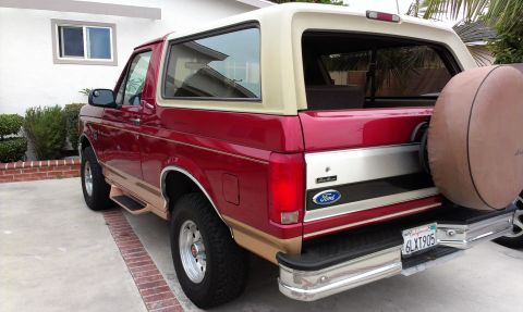 1994 Ford Bronco - Driver's-side rear three-quarter view of a red and tan two-tone full-size Ford Bronco with a tan removable hardtop, parked on a driveway be…