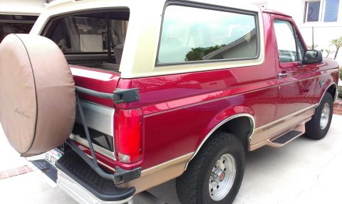 1994 Ford Bronco - Passenger-side rear three-quarter view of a red and tan two-tone full-size Ford Bronco with the tailgate down and the rear glass raised, pa…