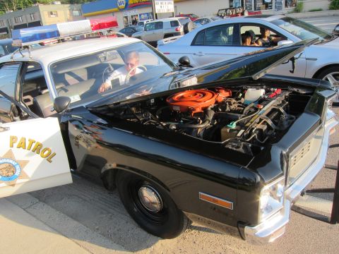 1991 Ford LTD Crown Victoria - Engine bay of a black-and-white Highway Patrol cruiser with the hood up, revealing a V8 engine with a bright orange air-cleaner cover.