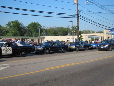 1991 Ford LTD Crown Victoria - lineup of vintage police cruisers, including Highway Patrol and State Police cars, parked along a roadside with a crowd and motorcycles beh…