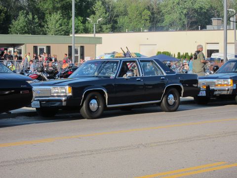 1991 Ford LTD Crown Victoria - black Ford full-size sedan, styled as an unmarked cruiser, parked along a road among classic cars and motorcycles at a public gathering.