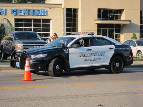 1991 Ford LTD Crown Victoria - black and white Johnston Police Ford interceptor with front push bar parked by a cone, a silver pickup behind it.