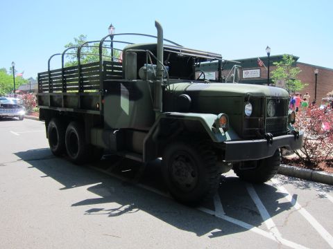 1991 Ford LTD Crown Victoria - olive drab military 6x6 cargo truck with stake-bed sides parked in a sunlit lot near a brick building.