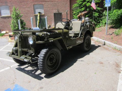 1991 Ford LTD Crown Victoria - olive drab military jeep with a helmet on the seat parked beside a brick building and an American flag.