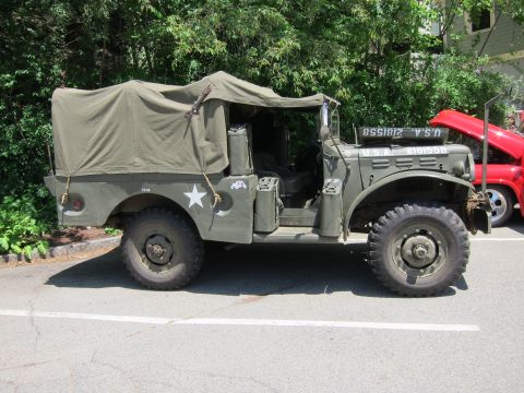 1991 Ford LTD Crown Victoria - Side view of an olive drab canvas-topped military truck bearing a white star, parked by a red vehicle.
