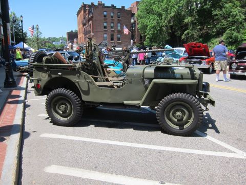 1991 Ford LTD Crown Victoria - Side view of an olive drab military jeep with hood serial numbers parked at a downtown car show.
