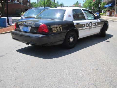 1991 Ford LTD Crown Victoria - Rear three-quarter view of a black-and-white Marlborough police sedan marked POLICE and EMERGENCY 911, parked on a downtown street.