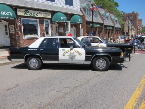 1991 Ford LTD Crown Victoria - vintage black-and-white Highway Patrol sedan with a gold star decal parked in front of Roc's barber shop downtown.