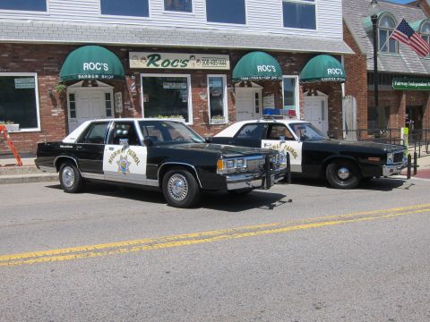 1991 Ford LTD Crown Victoria - Two vintage black-and-white Highway Patrol sedans with gold star decals parked at the curb downtown.