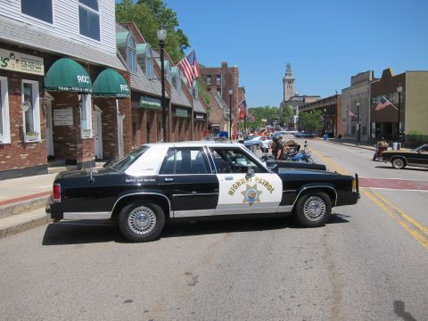 1991 Ford LTD Crown Victoria - black-and-white Highway Patrol sedan parked across a downtown street with a tower visible in the distance.