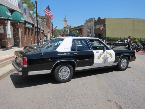 1991 Ford LTD Crown Victoria - Rear three-quarter view of a black-and-white Highway Patrol sedan with a gold star decal parked on a downtown street.