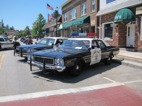 1991 Ford LTD Crown Victoria - Vintage black-and-white police sedans, including a Highway Patrol car, parked along a downtown street with US flags.