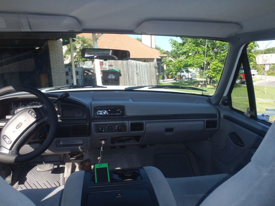 1997 Ford F-350 interior, gray dashboard, steering wheel, and seats. Green smartphone in center console