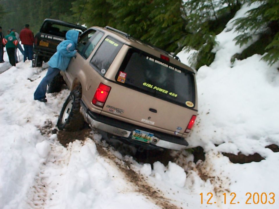 Tan Ford Explorer with GIRL POWER 4X4 decal stuck in snow on a trail, person in blue jacket beside it