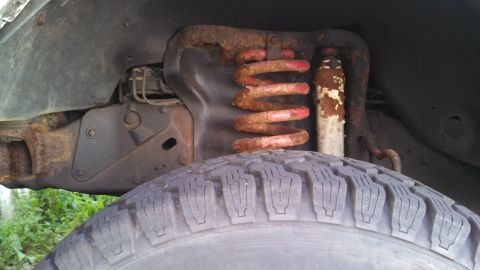 1993 Ford Bronco - Close-up view of the front suspension components, including a rusty coil spring and shock absorber.