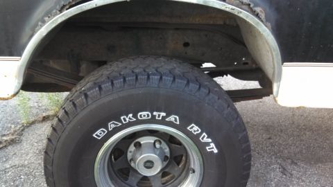 1993 Ford Bronco - Close-up of a vehicle's rear tire and wheel well shows rust and white trim.