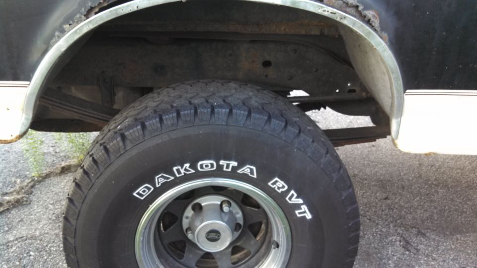 Black tire with white lettering 'DAKOTA RVT' on a vehicle with rusty wheel well and white trim