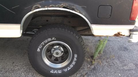 1993 Ford Bronco - This image shows the rear wheel well and tire of a black and white truck, with visible rust around the wheel arch.