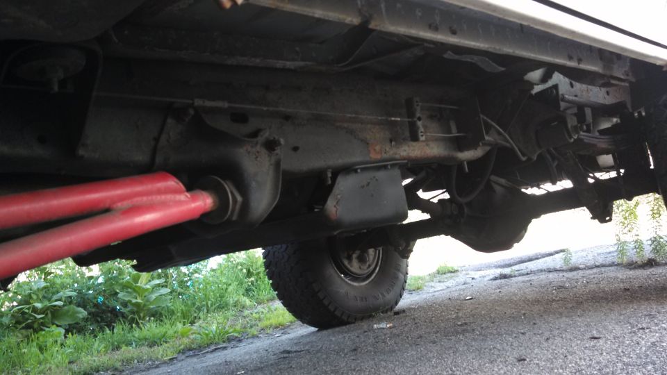 Underbody view of a vehicle showing red suspension arms and the rear axle