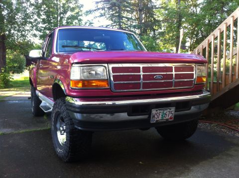 1992 Ford F-150 - Three-quarter front view of a magenta/raspberry ninth-generation Ford F-Series extended-cab pickup parked on a concrete driveway beside woo…