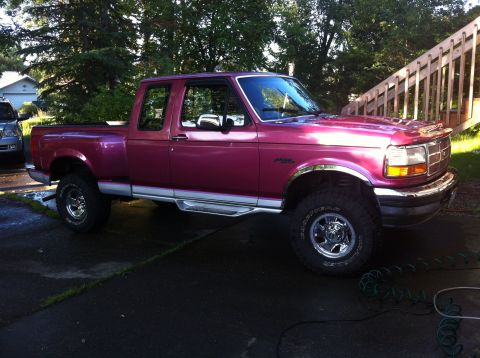 1992 Ford F-150 - Passenger-side 3/4 front view of a lifted burgundy OBS Ford extended-cab Flareside pickup on a wet driveway, with a coiled garden hose in t…