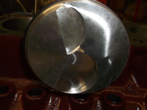 1970 Ford Mustang - Close-up of a piston with valve reliefs, positioned within a dark red engine block.